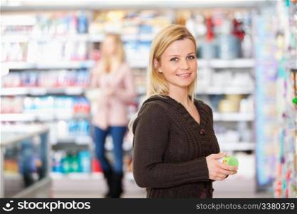 Young woman smiling while holding goods in the supermarket with people in the background
