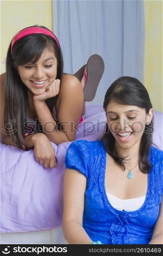 Young woman smiling with a teenage girl lying on the bed beside her