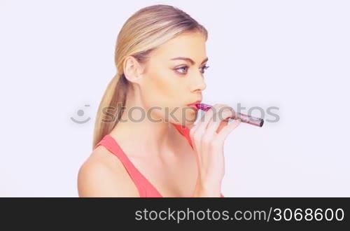 Young woman smoking an e-cigarette holding the vaporizer in her hands as she exhales a puff of smoke
