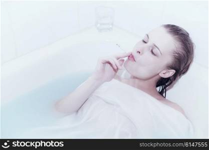Young woman smoking while lying in bathtub