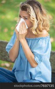 young woman sneezing outdoor while having an allergy