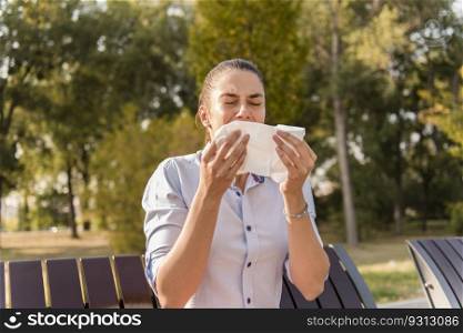 Young woman sneezing outdoor while having an allergy
