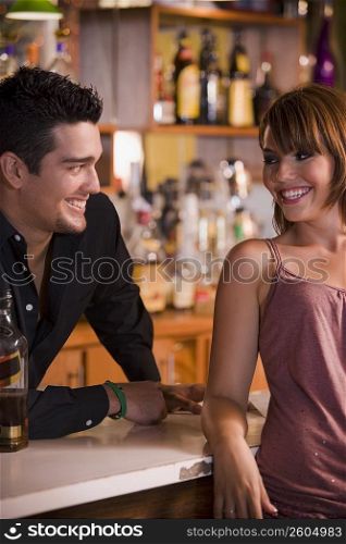 Young woman socializing with bartender at bar, night