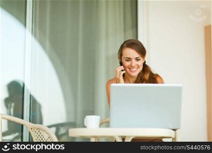 Young woman speaking mobile phone and looking in laptop