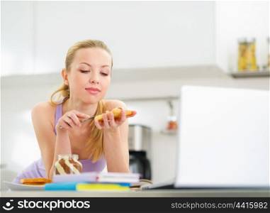 Young woman spread toast with chocolate cream while studying in kitchen
