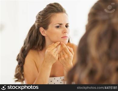 Young woman squeezing acne in bathroom
