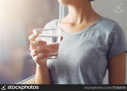 young woman standing and holding glass water near window. concept healthy