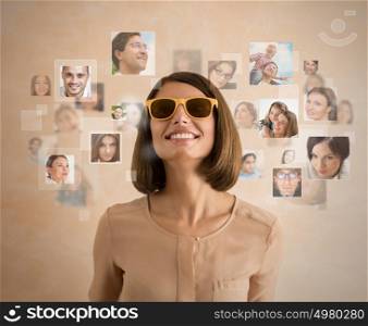Young woman standing and smiling with many different people's faces around her. Technology social media network of friends and communication.