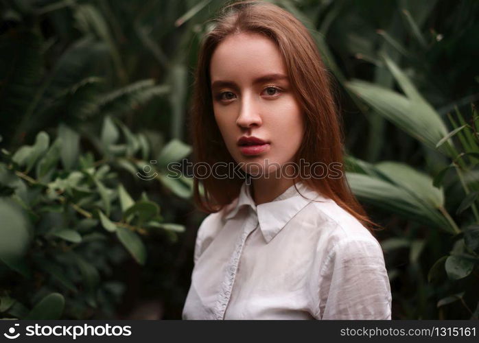 Young woman standing at a greenhouse with exotic plants and flowers.. Young woman standing at a greenhouse