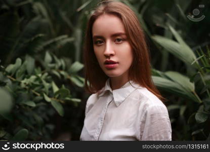 Young woman standing at a greenhouse with exotic plants and flowers.. Young woman standing at a greenhouse