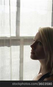 Young woman standing by window, close-up