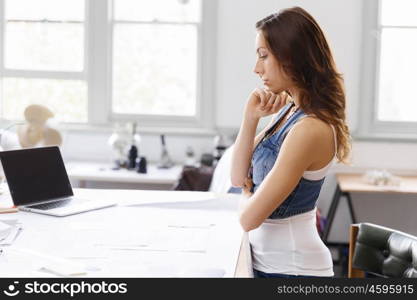 Young woman standing in creative office. Smiling young designer standing in creative office in front of her desk