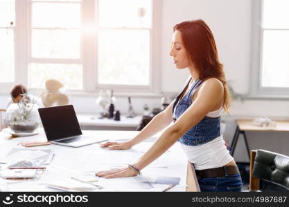 Young woman standing in creative office. Smiling young designer standing in creative office in front of her desk