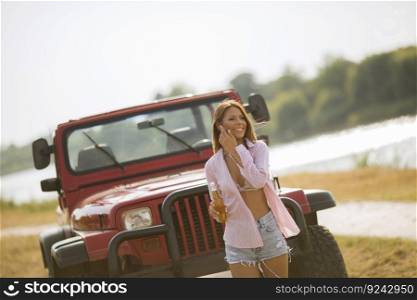 Young woman standing in front of red cabrio car near river