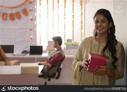 Young woman standing in office holding a box in hand during Diwali celebrations. 