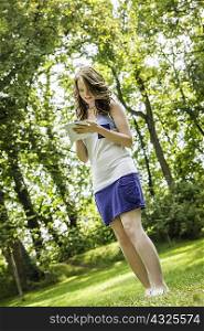 Young woman standing in park writing on notepad