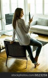 Young woman standing in the living room and using mobile phone