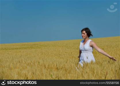 Young woman standing jumping and running on a wheat field with blue sky in background at summer day representing healthy life and agriculture concept