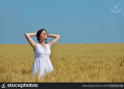 Young woman standing jumping and running on a wheat field with blue sky in background at summer day representing healthy life and agriculture concept