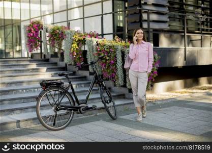 Young woman standing near ebike and uses smartphone outdoor