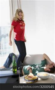 Young woman standing on a couch with a young man lying between her legs