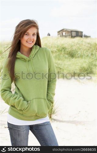 Young Woman Standing On Beach Wearing Hooded Top With Old Beach Hut In Distance