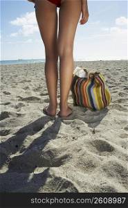 Young woman standing on beach with bag