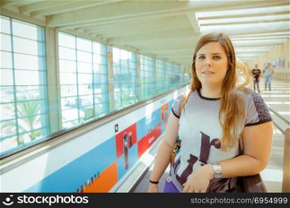 Young woman standing on escalator line in airport terminal and looking at camera.