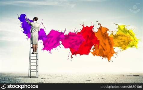 Young woman standing on ladder drawing splashes with finger