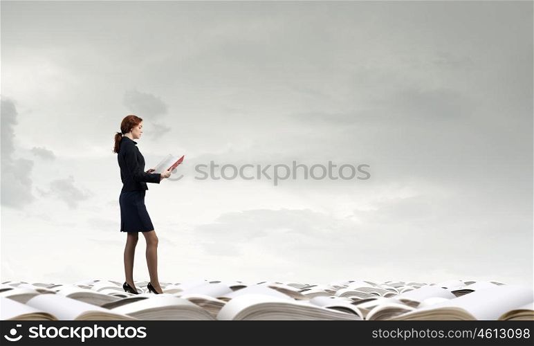 Young woman standing on pile of old books. Woman reading book