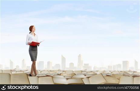 Young woman standing on pile of old books. Woman reading book