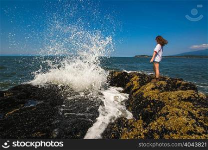Young woman standing on rocks by ocean, Bowen Island, British Columbia, Canada