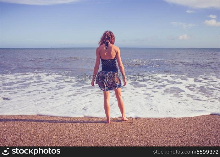 Young woman standing on the beach and dipping her feet