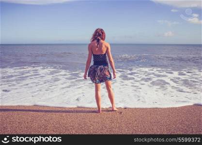 Young woman standing on the beach and dipping her feet