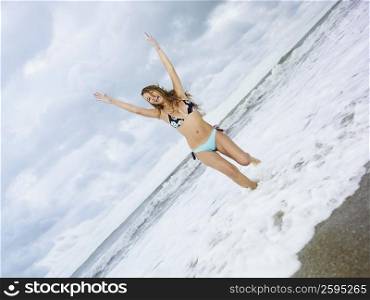 Young woman standing on the beach with her arms raised