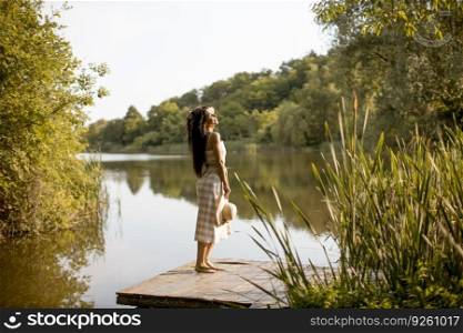 Young woman standing on the wooden pier at the calm lake on a hot summer day