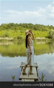 Young woman standing on the wooden pier at the calm lake on a hot summer day