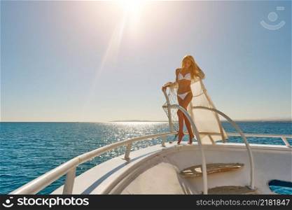 Young woman standing onth the deck of a boat in open sea at sunny summer day.. Young woman standing onth the deck of a boat in open sea at sunny summer day