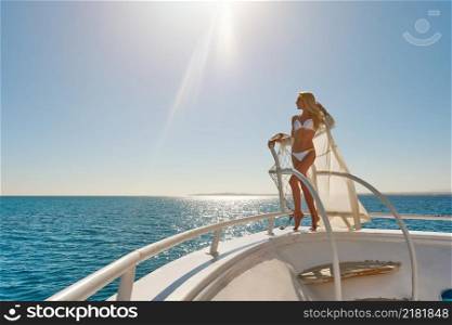 Young woman standing onth the deck of a boat in open sea at sunny summer day.. Young woman standing onth the deck of a boat in open sea at sunny summer day