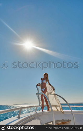 Young woman standing onth the deck of a boat in open sea at sunny summer day.. Young woman standing onth the deck of a boat in open sea at sunny summer day