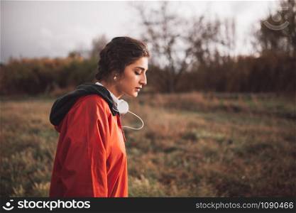 Young woman standing with raincoat and headphones on the field in a rainy day