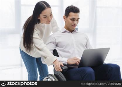 young woman standing young man sitting wheelchair using laptop