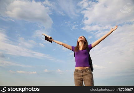 Young woman staying with raised hands against blue sky