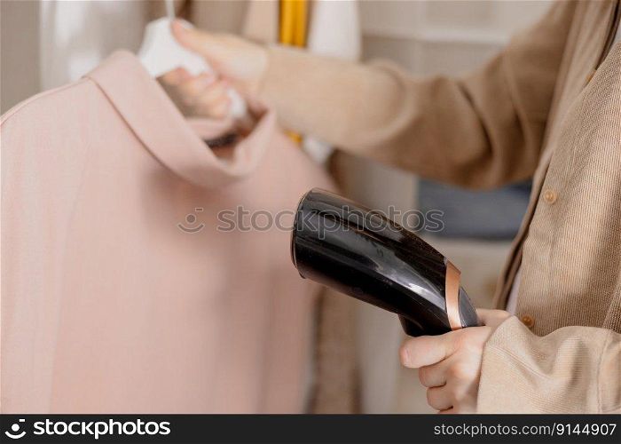 Young woman steaming her clothes at home, close up view. Female using electric steamer, ironing clothes on hanger. Modern technologies. Young woman steaming her clothes at home, close up view. Female using electric steamer, ironing clothes on hanger. Modern technologies.