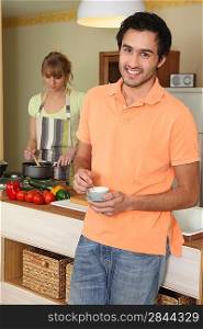 Young woman stirring into saucepan and man holding cup of coffee