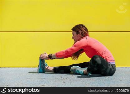 young woman stretching on the floor in front of a yellow wall before running