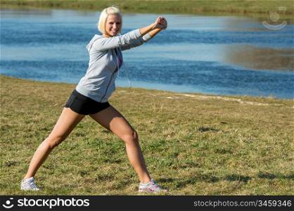 Young woman stretching outdoors before jogging workout by park lake