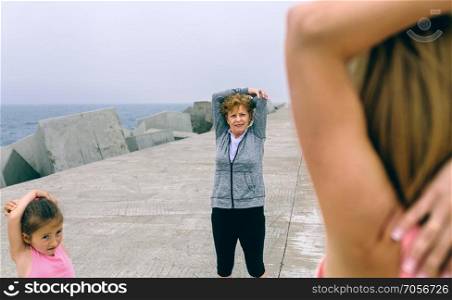 Young woman stretching with girl and senior woman by sea pier. Woman stretching with girl and senior woman