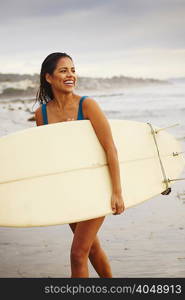 Young woman strolling on beach carrying surfboard, San Diego, California, USA