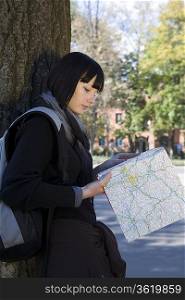 Young woman study map leaning on tree
